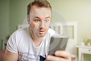 Caucasian white young man looking shocked at his phone with big opend eyes.