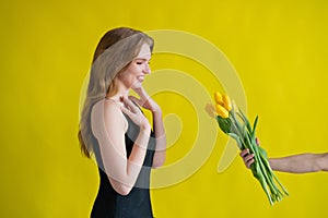 Caucasian woman accepts tulips as a gift on yellow background. photo