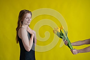 Caucasian woman accepts tulips as a gift on yellow background. photo