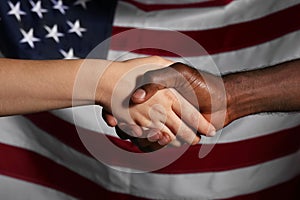 Caucasian woman and African-American man shaking hands near national flag of USA. Racism concept