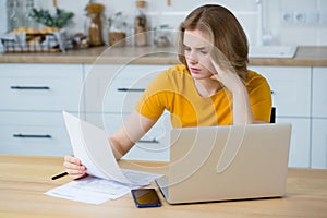 Caucasian woman analyzing budget or utility bills, looking worried sitting at home at the kitchen