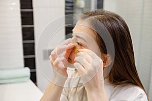 Caucasian woman applying hydrogel patches on under eye area, looking at mirror. Happy young lady enjoying morning anti