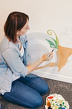 Caucasian woman artist hand painting murals on walls indoor at apartment or studio school with the acrylic paints. Lifestyle