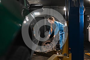 Caucasian woman auto mechanic works on tire fitting in a car service station. Portrait of an auto mechanic changing a