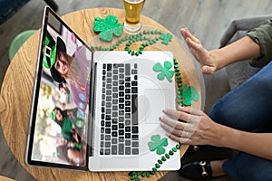 Caucasian woman at bar making st patrick's day video call waving to friend in costume on laptop