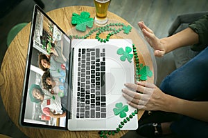 Caucasian woman at bar making st patrick's day video call waving to group of friends in on laptop