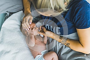 Caucasian woman with blond hair lying in bed with her newborn baby boy caressing his head and letting him suck her thumb