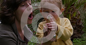 Caucasian woman blowing on flower with baby in garden