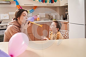 Caucasian woman blowing at the party pipe while preparing celebrating birthday of her son