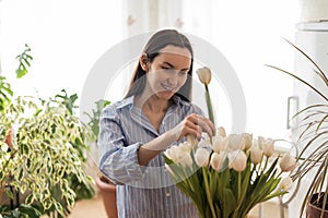 Caucasian woman in blue shirt caring for white tulips in vase, nature-inspired environments, spring, cozy and comfort home