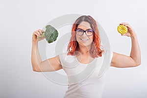 Caucasian woman chooses between vegetables and fast food. Redhead girl holding broccoli and donut on a white background.