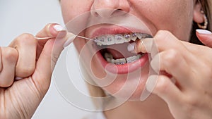 Caucasian woman cleaning her teeth with braces using dental floss. Cropped portrait.