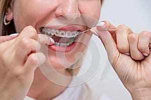 Caucasian woman cleaning her teeth with braces using dental floss. Cropped portrait.