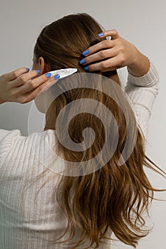 Caucasian woman clipping her long blond wavy hair hair with a pearly snap hair clip.