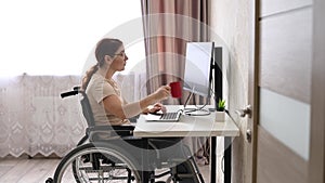 Caucasian woman with disabilities working at the computer while sitting in a wheelchair.