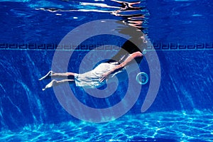 Caucasian woman diving in swimming pool wearing white dress.underwater view. Summer time and vacation concept