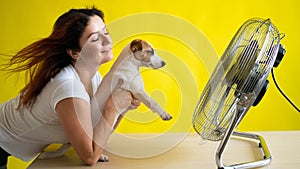 Caucasian woman and dog are cooled by an electric fan. A girl with her pet Jack Russell Terrier freshens up