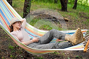 Caucasian woman drinks hot tea from a thermo mug while lying in a hammock in nature.