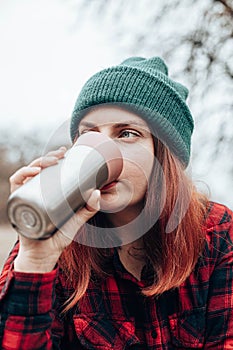 Caucasian woman drinks from a mug of thermos. Rest at in nature autumn forest