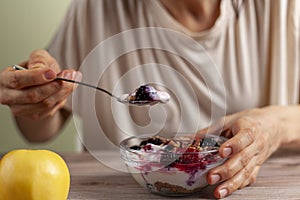 caucasian woman is eating a fresh home made glass bowl of creamy yogurt parfait