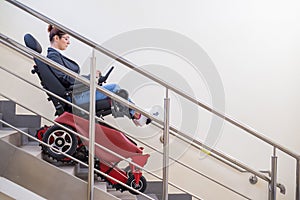 Caucasian woman in electric caterpillar wheelchair climbs up stairs.