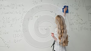 Caucasian woman erasing formulas from white board.