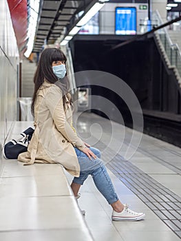 Caucasian woman with face mask sitting inside a subway station