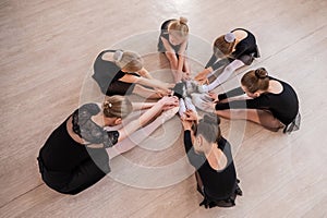 Caucasian woman and five little girls sit in a circle and do stretching at a ballet school.