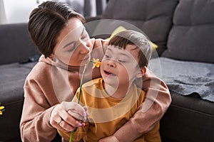 Caucasian woman giving smells flower to her son with down syndrome