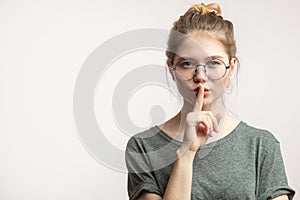 Caucasian woman with hair bun keeping index finger at lips, isolated over white.