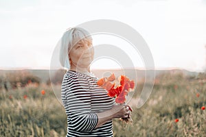 Caucasian woman hand holding a bouquet of poppy flower on meadow background at sunset