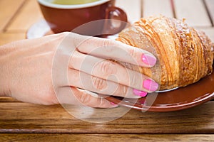 Caucasian woman hand touching buttery croissant in cafe on wooden table background