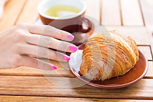 Caucasian woman hand touching buttery croissant in cafe on wooden table background