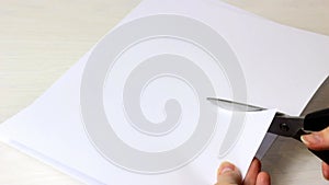 Caucasian woman hands cutting the sheet of paper with the scissors on light wooden table