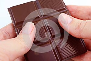 Caucasian woman hands holding and breaking off chocolate from a bar close up.