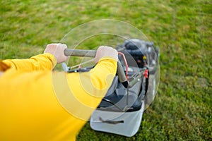 Caucasian woman hands using electric lawn mower while working at garden.