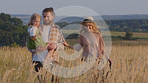 Caucasian woman in hat and bearded man with small girl walk in park nature family walking in wheat field outdoors