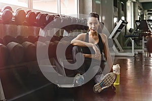 Caucasian woman having relax after workout and excercise in gym and fitness club with roll of dumbells on rack, healthy sports photo