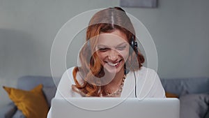 Caucasian woman with headset talking and laughing looking into laptop.