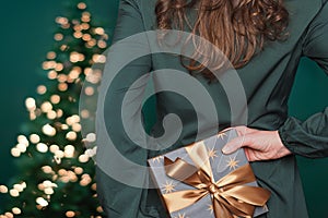 Caucasian woman hiding gift box with golden ribbon behind her back