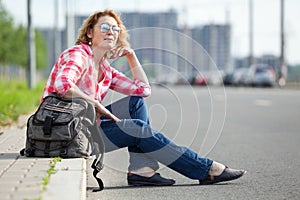 Caucasian woman hitch a ride on empty road, alone traveler sitting on roadside and waiting the car