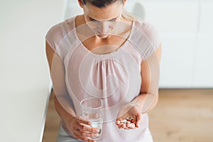 Caucasian woman holding a bunch of pills in one hand and a glass of water in other, top down view