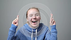 Caucasian woman holding fingers crossed shouting isolated on gray background