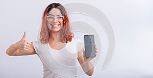 Caucasian woman holding phone with blank screen and showing thumb up on white background.