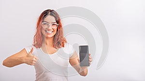 Caucasian woman holding phone with blank screen and showing thumb up on white background.