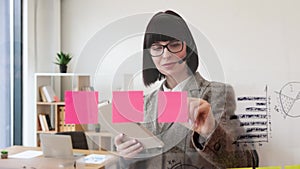 Caucasian woman holding tablet in hand standing near transparent office board.