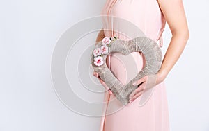 Caucasian woman holds in two hands a heart made of burlap with pink flowers embellishment. Body only, no head