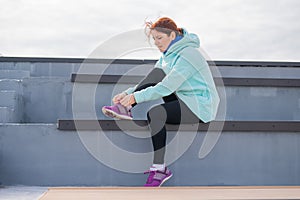 Caucasian woman in a hoodie tying her shoelaces before jogging.