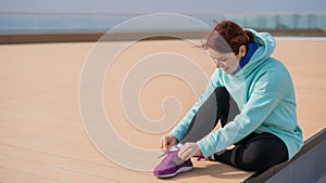 Caucasian woman in a hoodie tying her shoelaces before jogging.