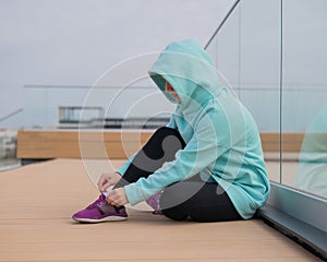 Caucasian woman in a hoodie tying her shoelaces before jogging.